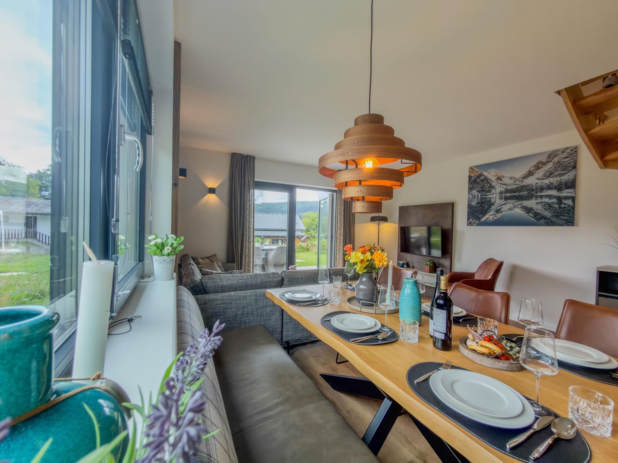 A modern dining area with a wooden table set for a meal, a sofa, and a view of the outdoors.