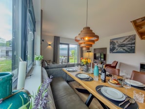 Un espace de repas moderne avec une table en bois dressée pour un repas, un canapé et une vue sur l’extérieur.
