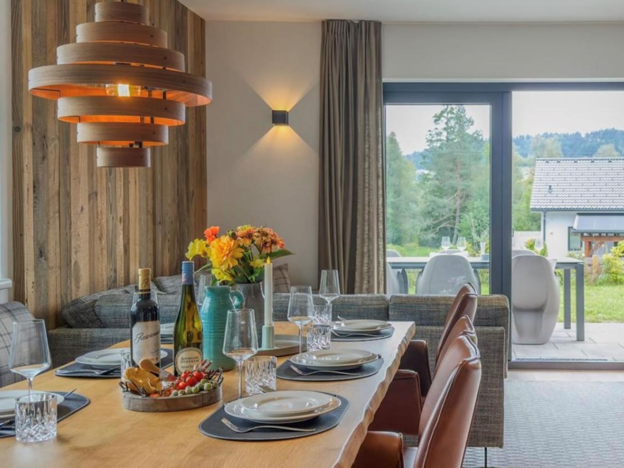 A dining area with a wooden table set for a meal, a vase of flowers, and a bottle of wine.
