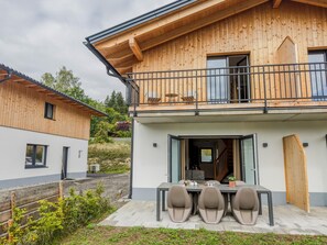Une maison moderne en bois, dotée d’un balcon, d’un coin repas avec des chaises et d’une cuisine ouverte.