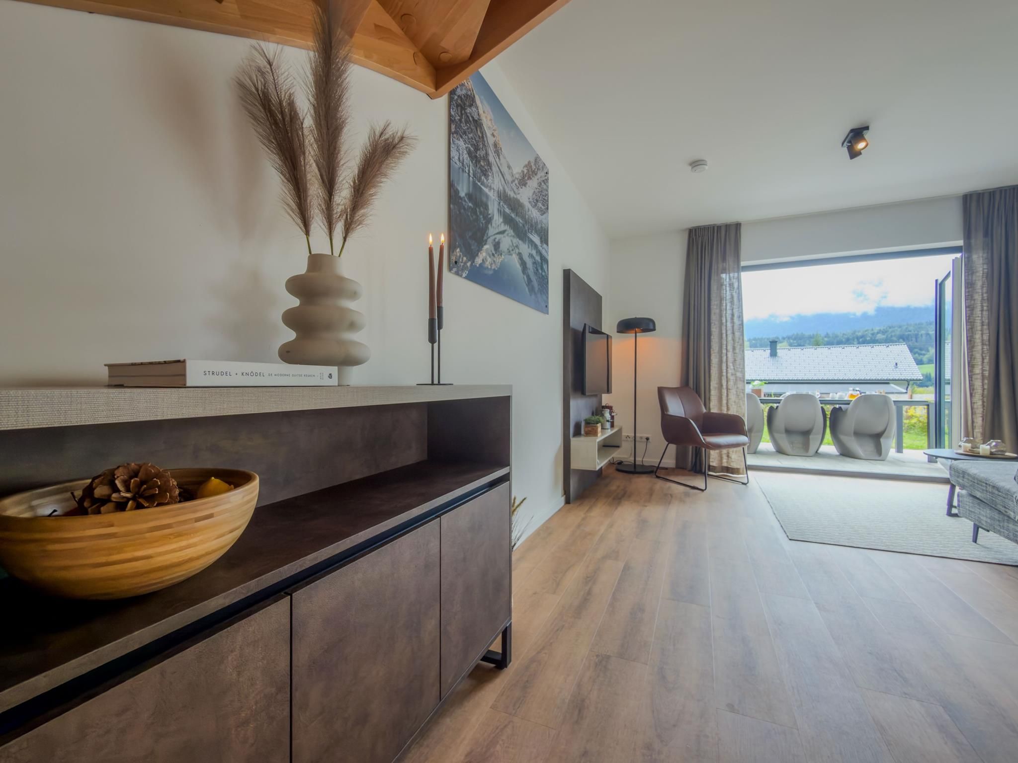 A modern living room with a wooden floor, a dark-toned console table, a vase with pampas grass, and a framed picture on the wall.