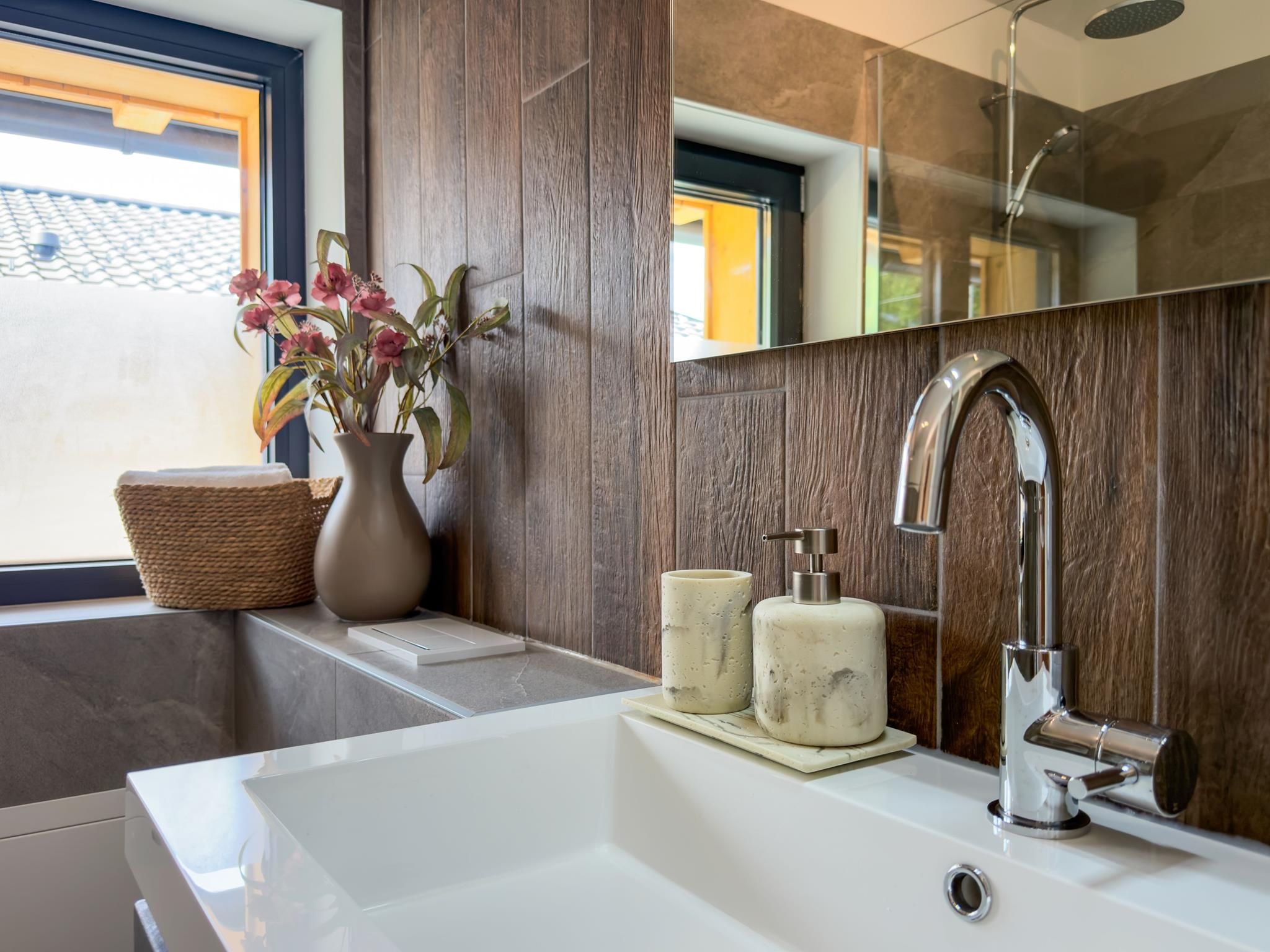 A modern bathroom with a large mirror, a white sink, and a shower.