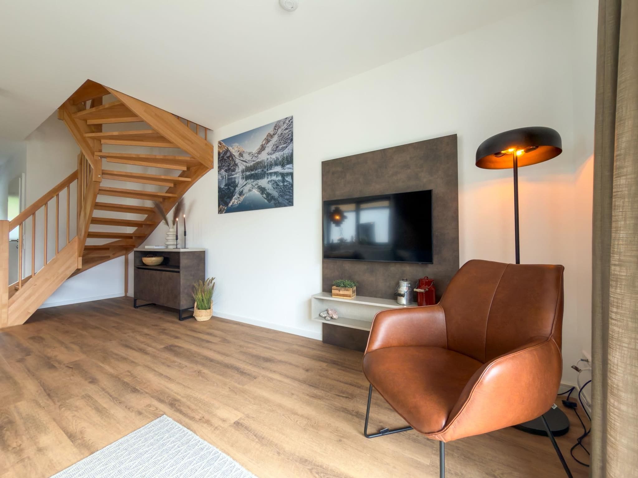 Un salon moderne avec un escalier en bois, un téléviseur à écran plat, un fauteuil en cuir et une lampe sur pied.