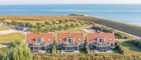 A large, modern house with a red roof, multiple balconies, and a view of the sea.