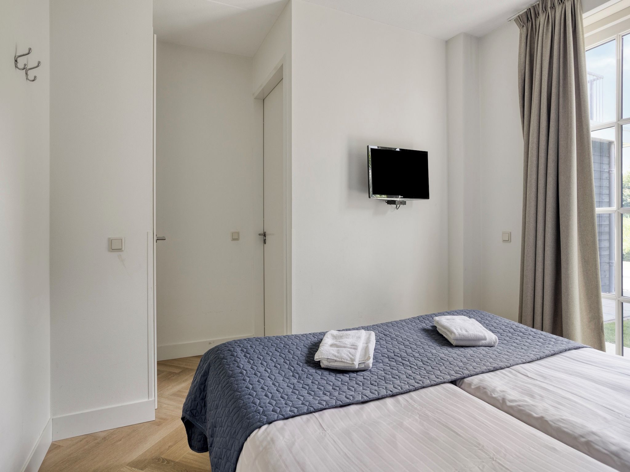 A hotel room with a bed, a TV mounted on the wall, and a window with curtains.