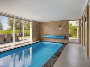 Ein Swimmingpool mit klarem, blauem Wasser, umgeben von beige gefliesten Wänden und einer Glastür, die nach draußen führt.