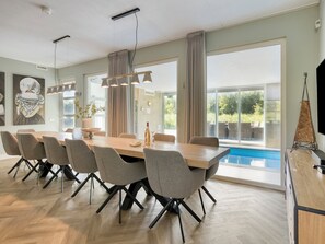 Un vaste espace dédié à la salle à manger, avec une grande table et des chaises modernes, de grandes fenêtres agrémentées de rideaux et une vue sur une piscine.