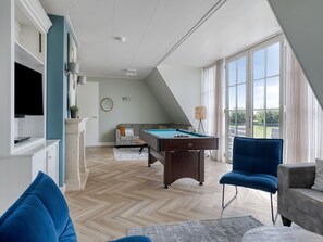 Ampla sala de estar com mesa de bilhar, televisão e uma grande janela com vista para o exterior.