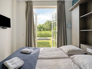 Ein Schlafzimmer mit Bett, Fernseher und Blick auf einen Garten.