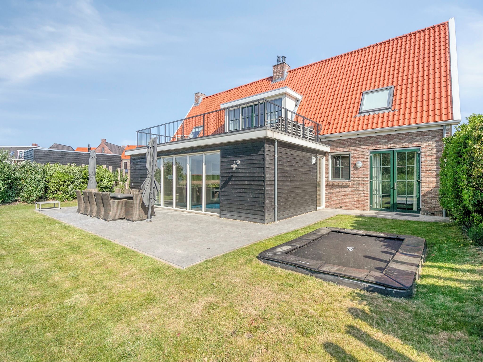 A modern two-story house with a red-tiled roof, a balcony, and a backyard with a trampoline.