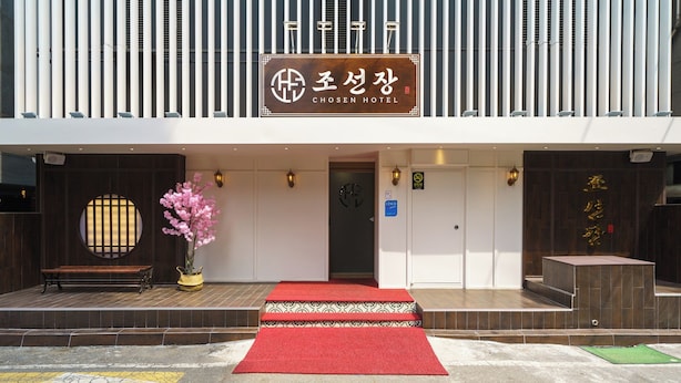 A hotel entrance with a red carpet, a wooden bench, and a potted plant. - Incheon Bupyeong Chosunjang (Incheon)