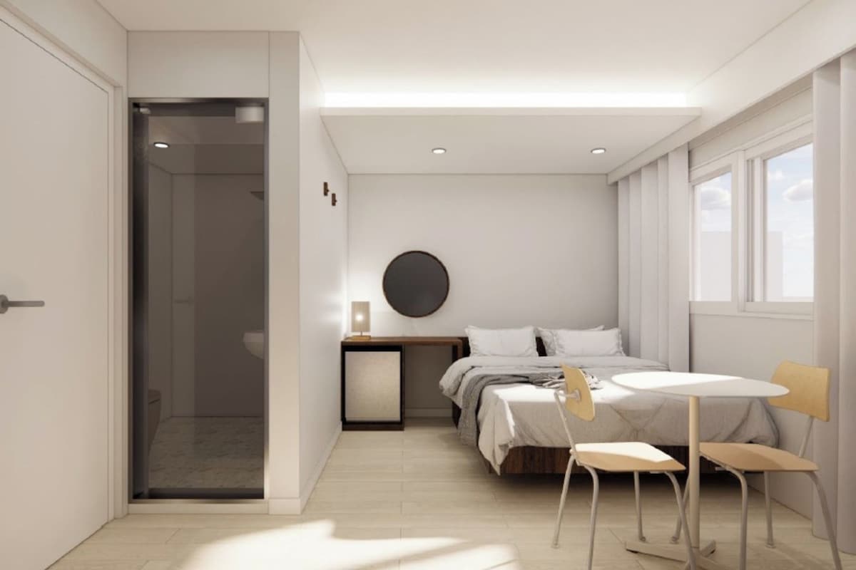 A modern bedroom with a bed, bedside table, lamp, and a small table with chairs.