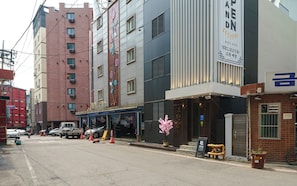A street view with a building featuring a large sign, a parked car, and a pedestrian crossing. - Incheon Bupyeong Chosunjang (Incheon)