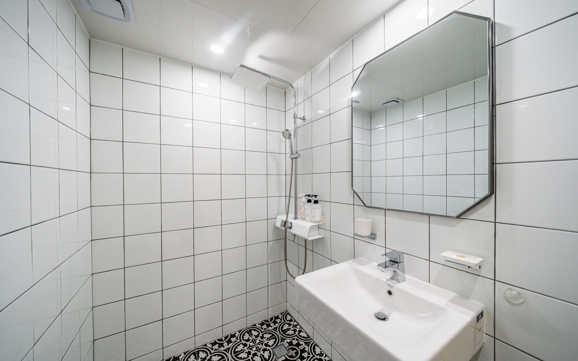 Un baño con azulejos blancos, un lavabo blanco, un espejo y una ducha.