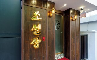 A hotel entrance with wooden paneling, illuminated signage, and a red carpet leading to the door.