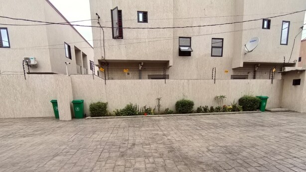 A courtyard with a paved floor, green trash bins, and a building with multiple windows and balconies. - Tranquil & Elegant 2-bedroom townhome in Accra, minutes from airport and malls (Accra)