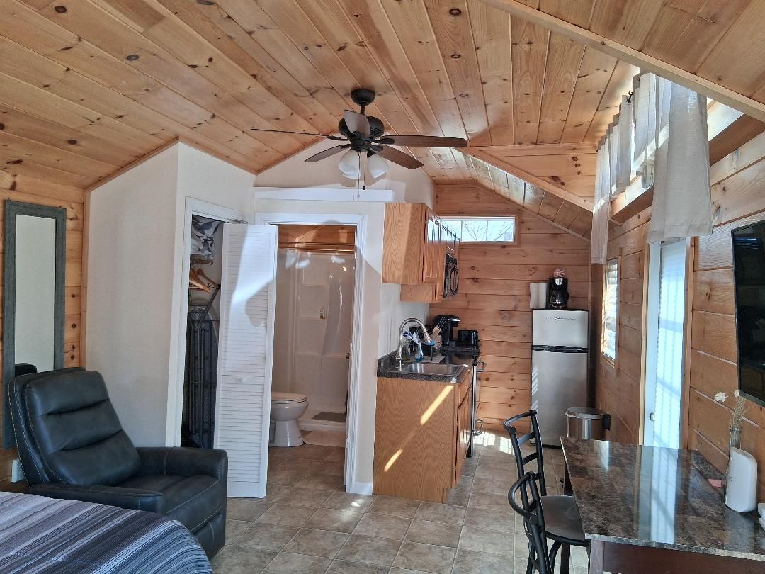 A wooden interior with a ceiling fan, a kitchen area with a refrigerator, and a dining space with a table and chairs.
