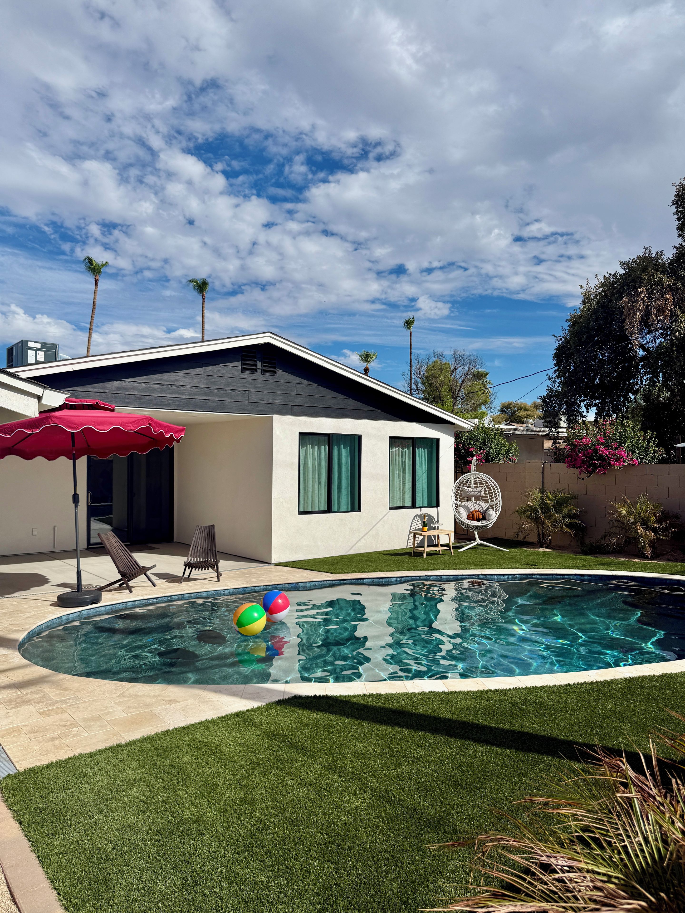 A modern house with a swimming pool, a patio with chairs, and a red umbrella.
