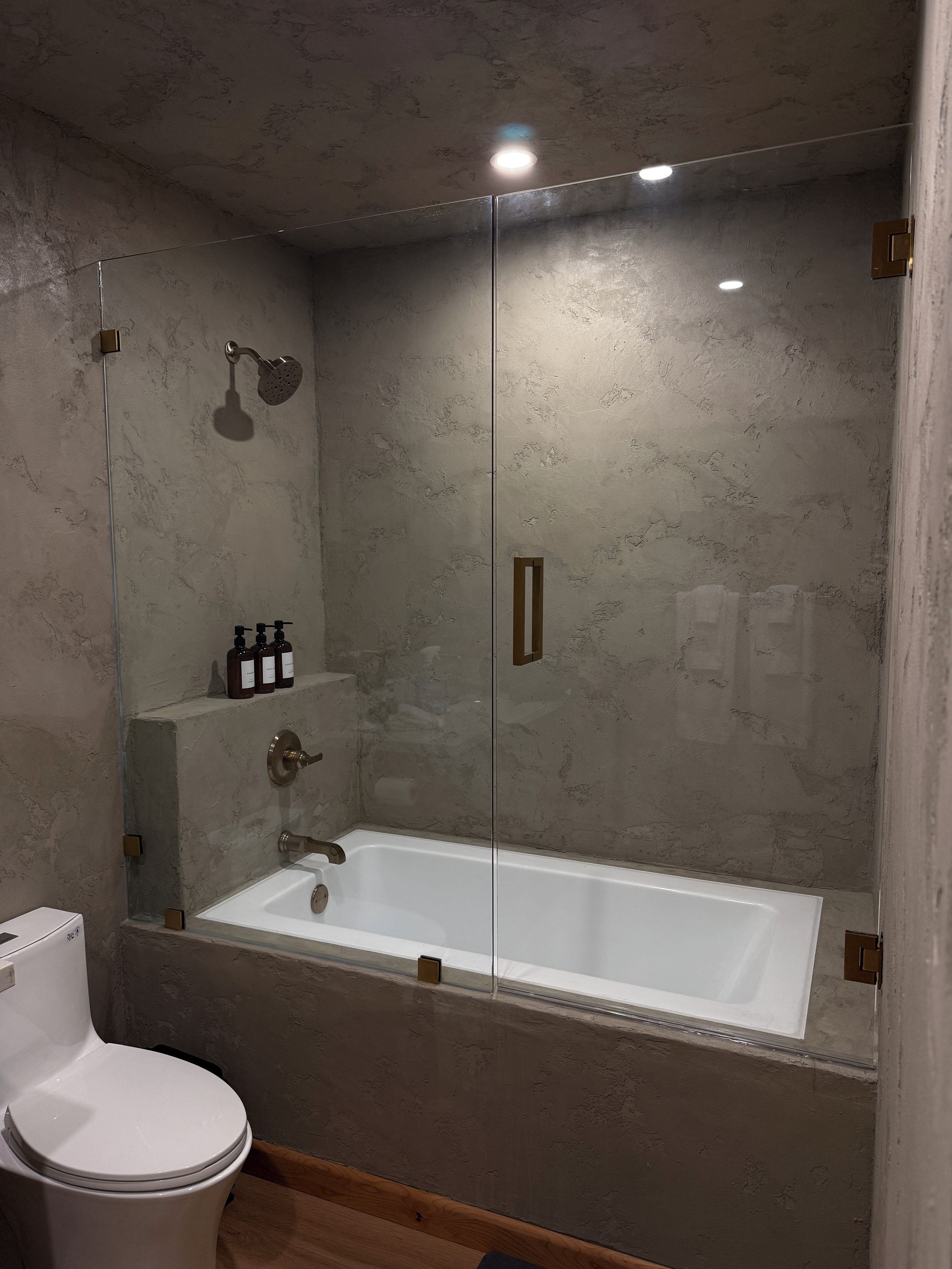 A modern bathroom with a glass-enclosed shower, a white bathtub, and a toilet.