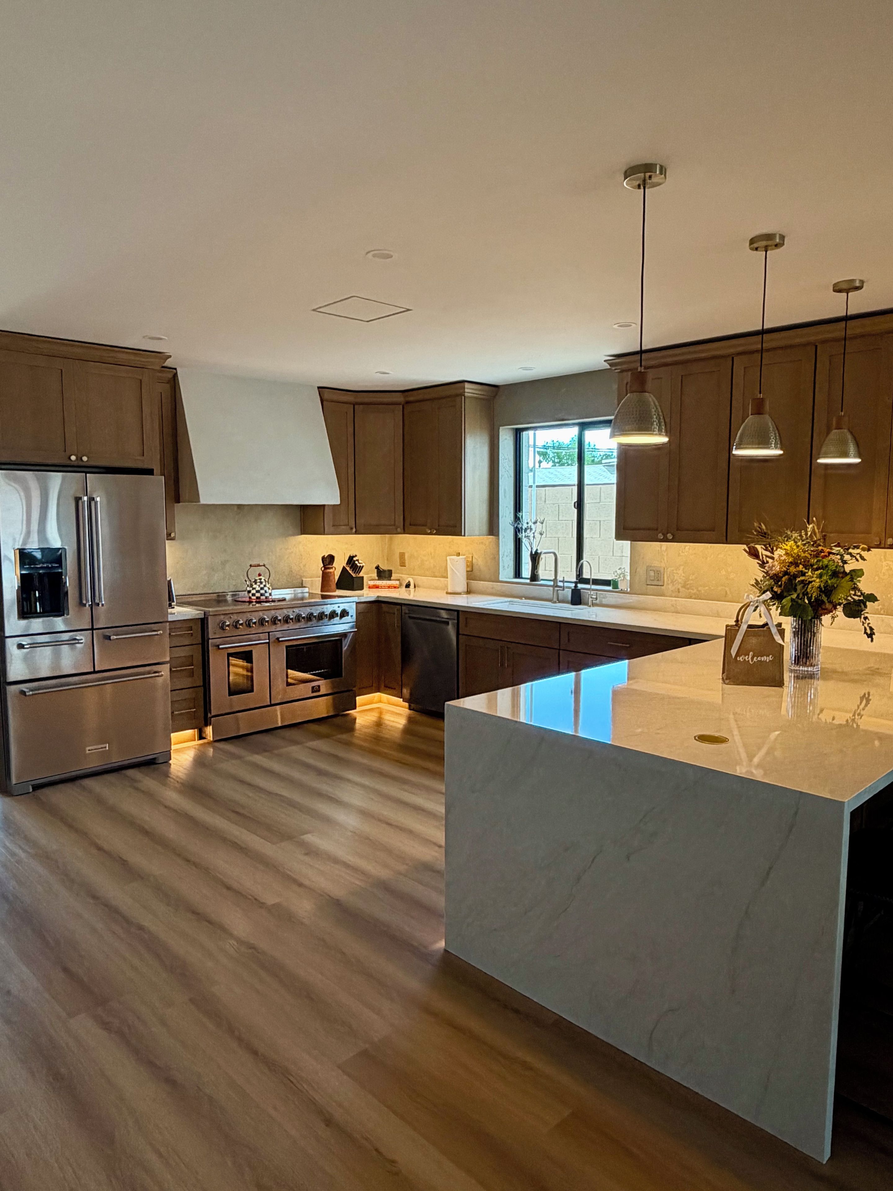 A modern kitchen with a central island, stainless steel appliances, wooden cabinets, and pendant lighting.