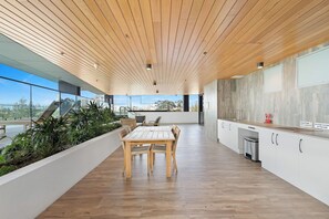 A modern kitchen with wooden flooring, a dining area with a table and chairs, and a view of the cityscape through large windows. - Oceanview Oasis - Games, Views, Vibes (Southport)