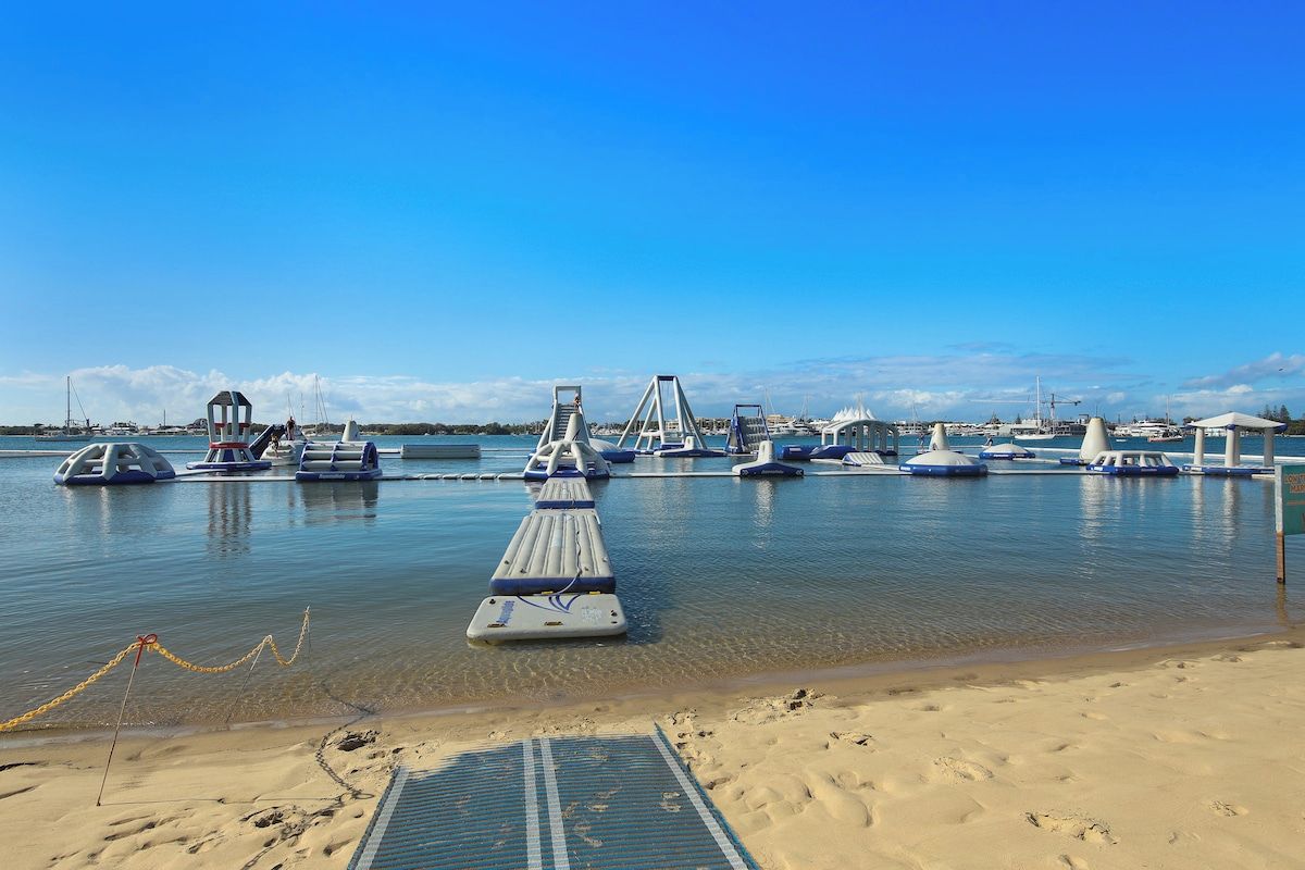 Eine Marina mit vertäuten Booten, ein Sandstrand und ein klarer, blauer Himmel.
