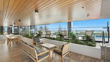 A modern lounge area with wooden flooring, wicker furniture, and a view of the sea.