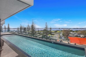 A swimming pool with a clear view of a body of water and trees in the background. - Oceanview Oasis - Games, Views, Vibes (Southport)
