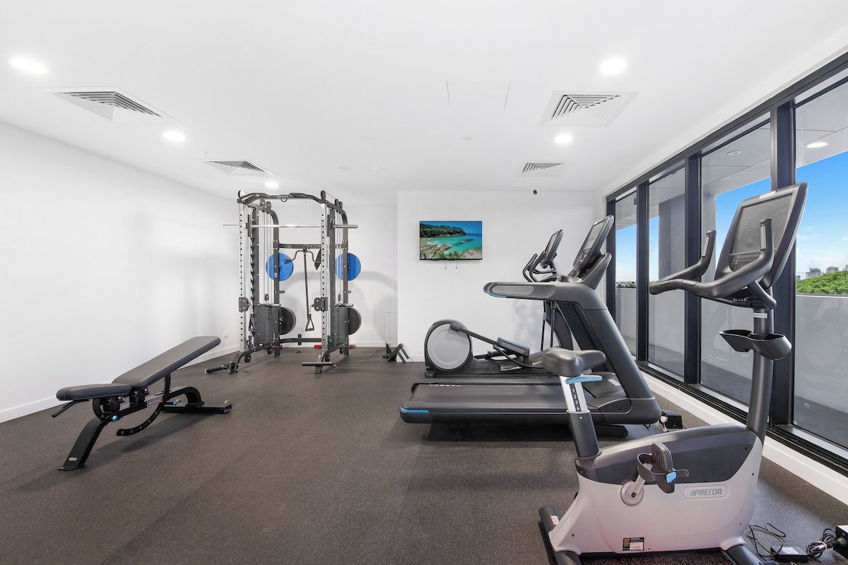 Ein Fitnessstudio mit Cardiogeräten, Kraftstationen und einer Bank.