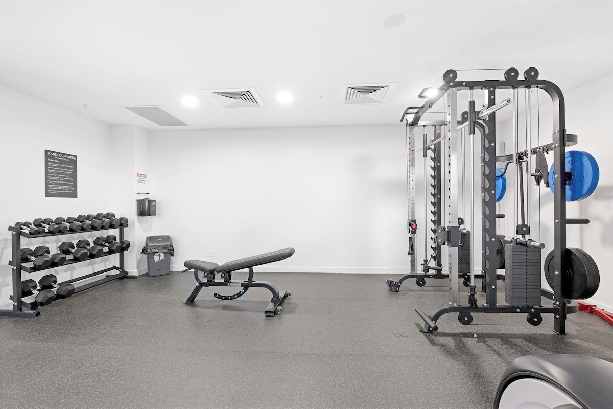 A gym with weightlifting equipment, a bench, and dumbbells.