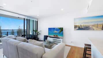 A modern living room with a large window overlooking a body of water, a flat-screen TV, and a dining area.