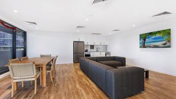 A modern living room with a wooden dining table and chairs, a grey sofa, and a kitchen in the background.