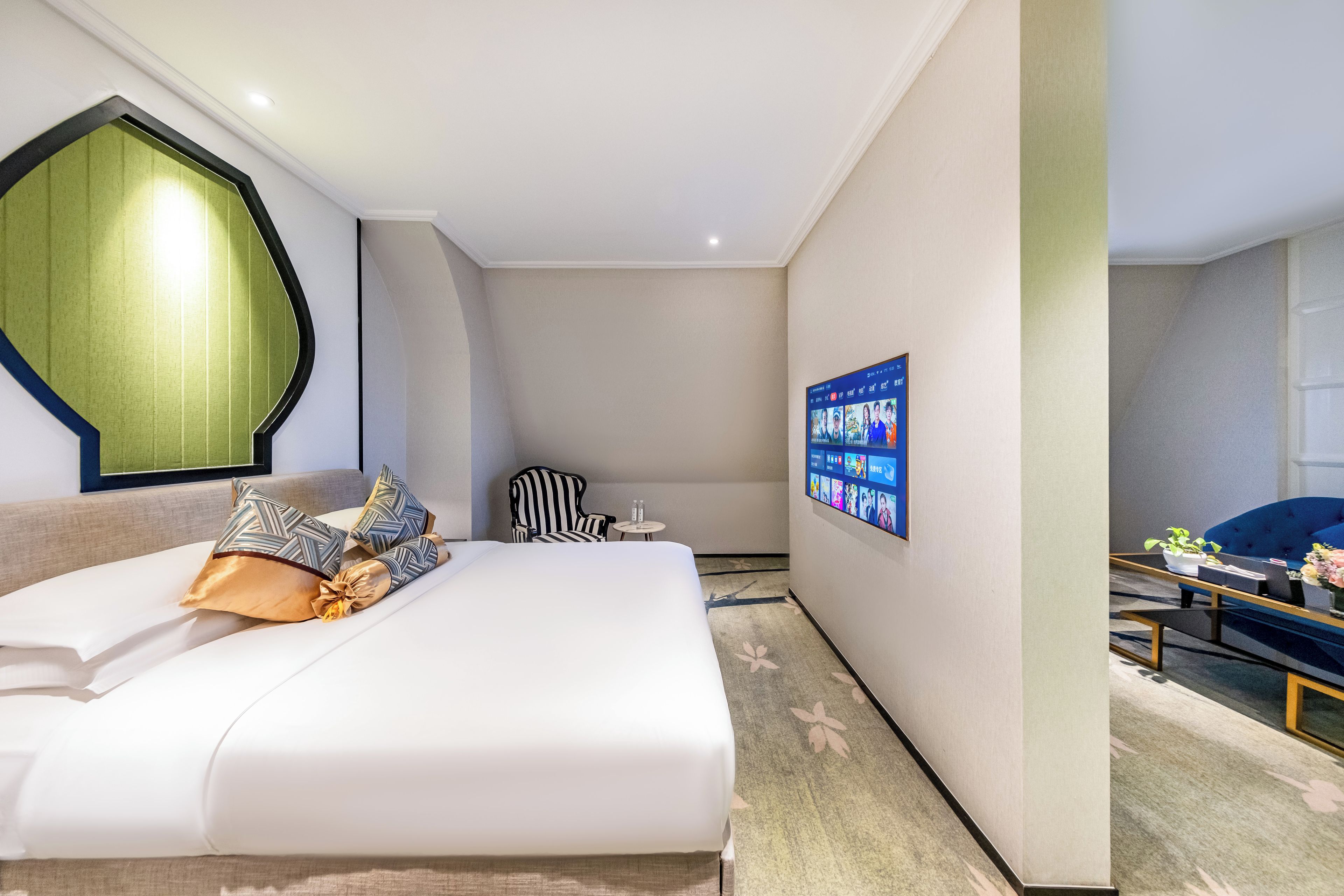 Habitación de hotel con cama, una silla, una mesita y televisor montado en la pared.