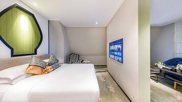 Habitación de hotel con cama, una silla, una mesita y televisor montado en la pared.