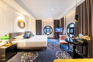 Quarto de hotel com cama, escrivaninha, cadeira, televisão e janela.