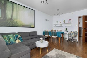 A modern living room with a grey sofa, a round white coffee table, and a large forest-themed painting on the wall.