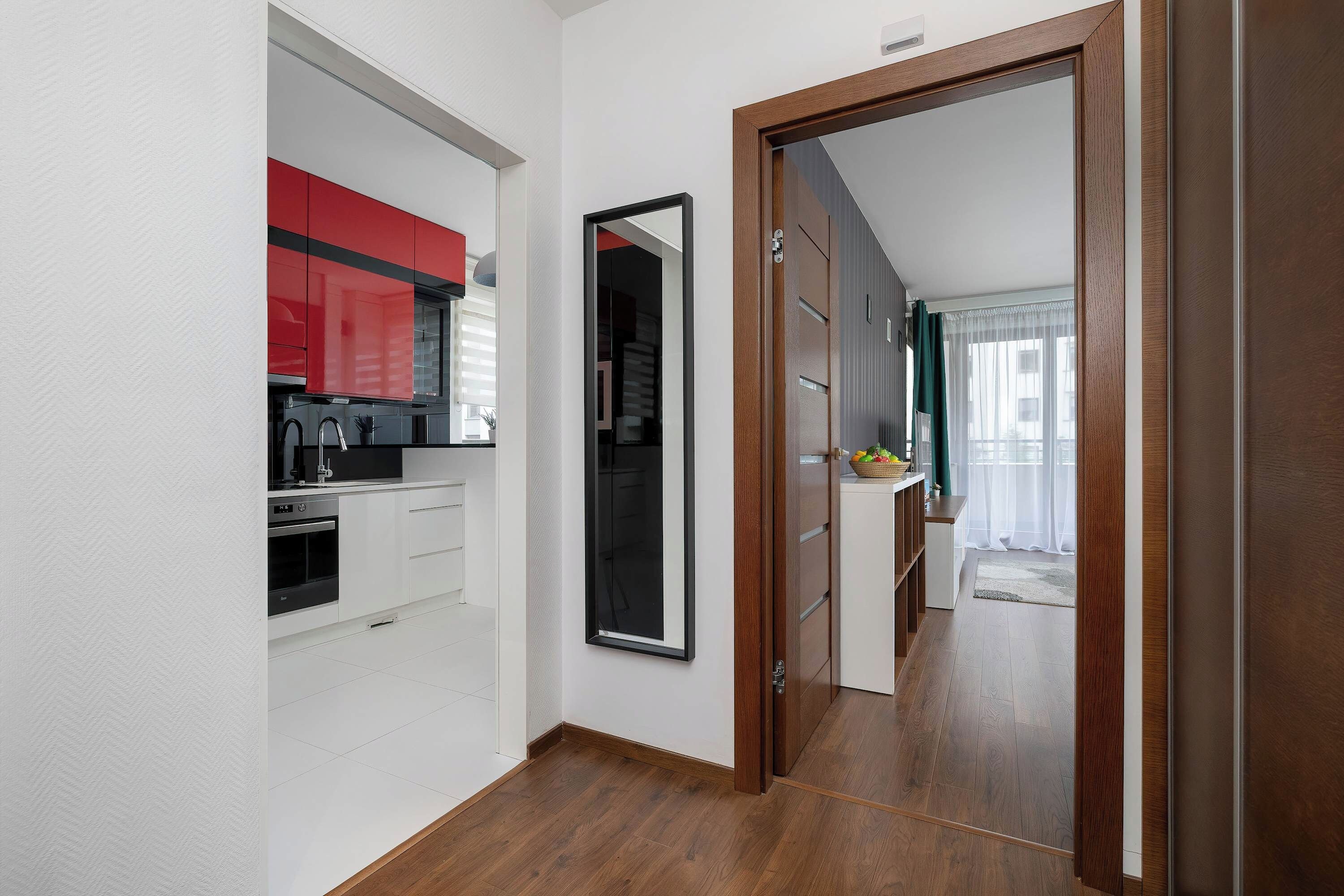 A modern kitchen with white cabinetry, a red accent wall, and a built-in oven.