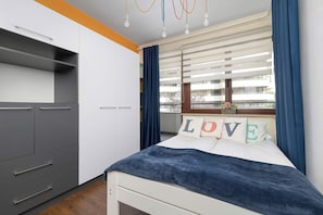 A bedroom with a bed, a wardrobe, a window with curtains, and a view of the outside.