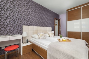 Quarto de hotel com cama, mesa de cabeceira, luminária e escrivaninha com cadeira.