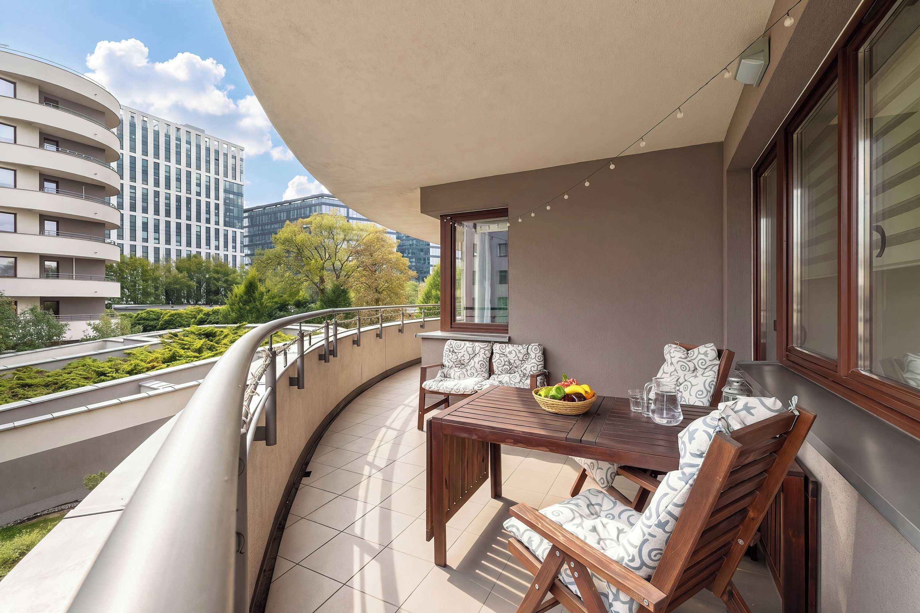 Un balcon avec une table et des chaises, un panier de fruits et une carafe.