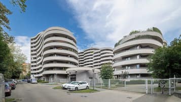 Un bâtiment moderne à plusieurs étages, doté d’une façade incurvée, d’un espace de stationnement avec des voitures et d’un ciel dégagé.