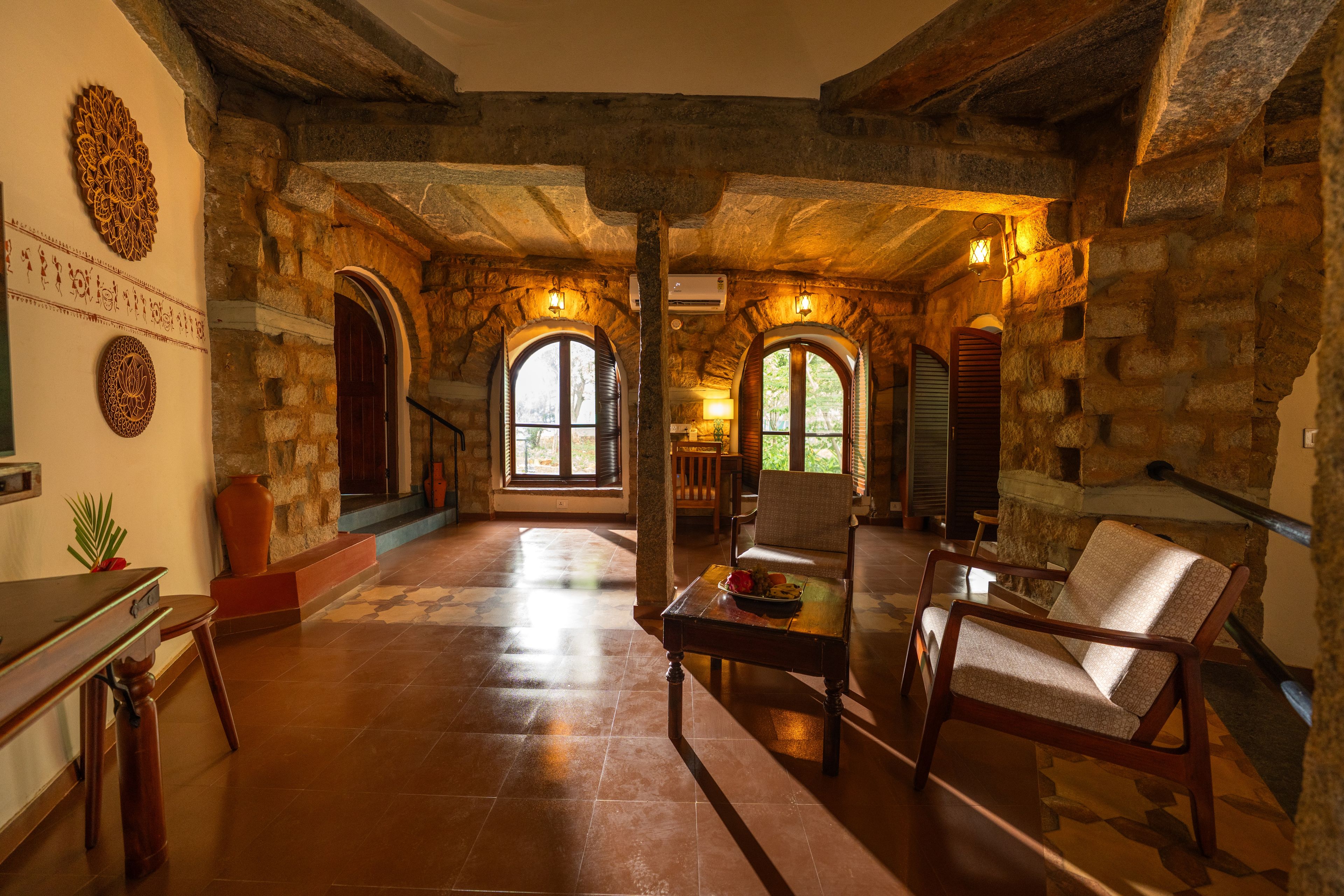 Un intérieur spacieux avec des murs en pierre, des portes en arc de cercle et un espace de détente central agrémenté d’une table et de chaises.
