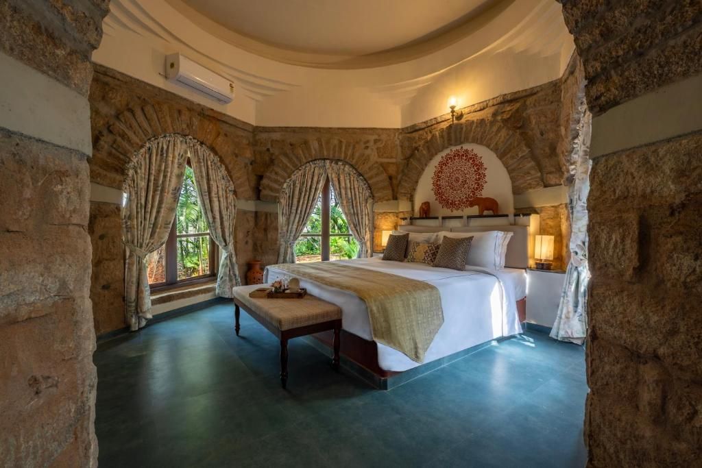 A bedroom with a large bed, a bench, and a stone wall.