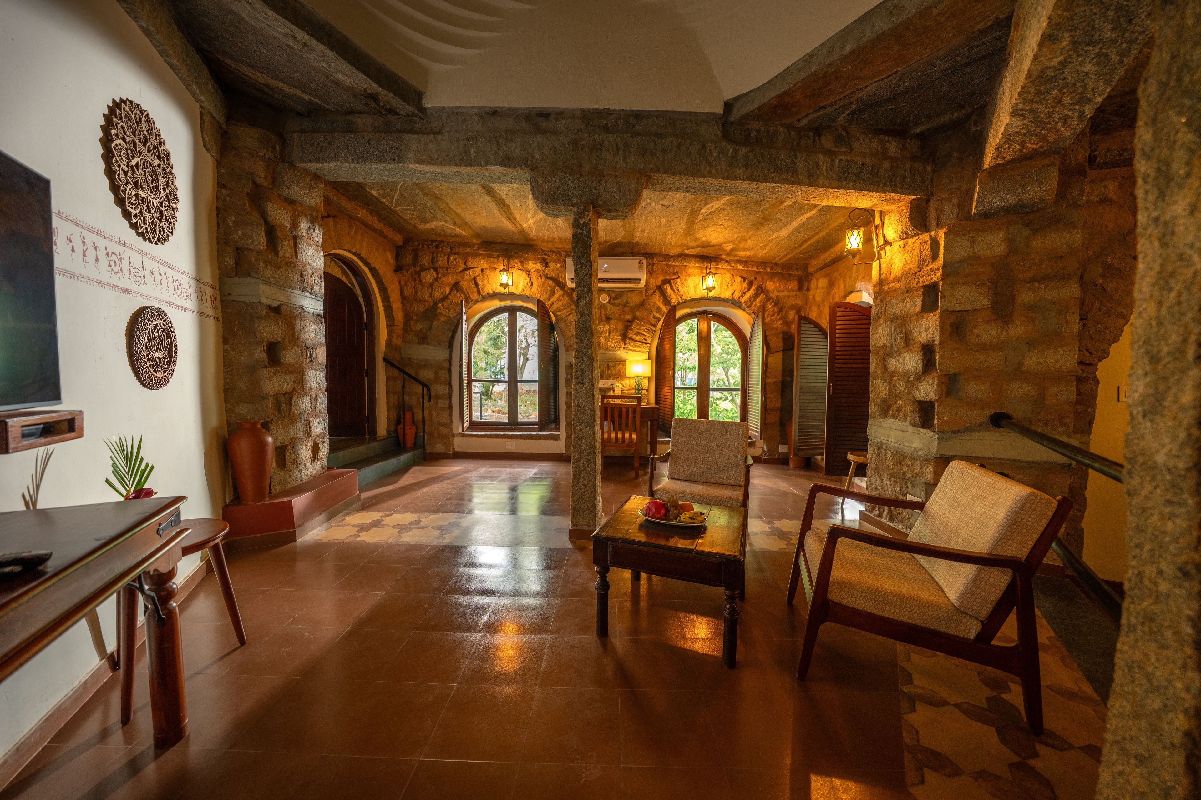 A spacious room with stone walls, a wooden floor, and a large arched window allowing natural light.