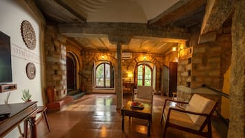 A spacious room with stone walls, a wooden floor, and a large arched window allowing natural light.