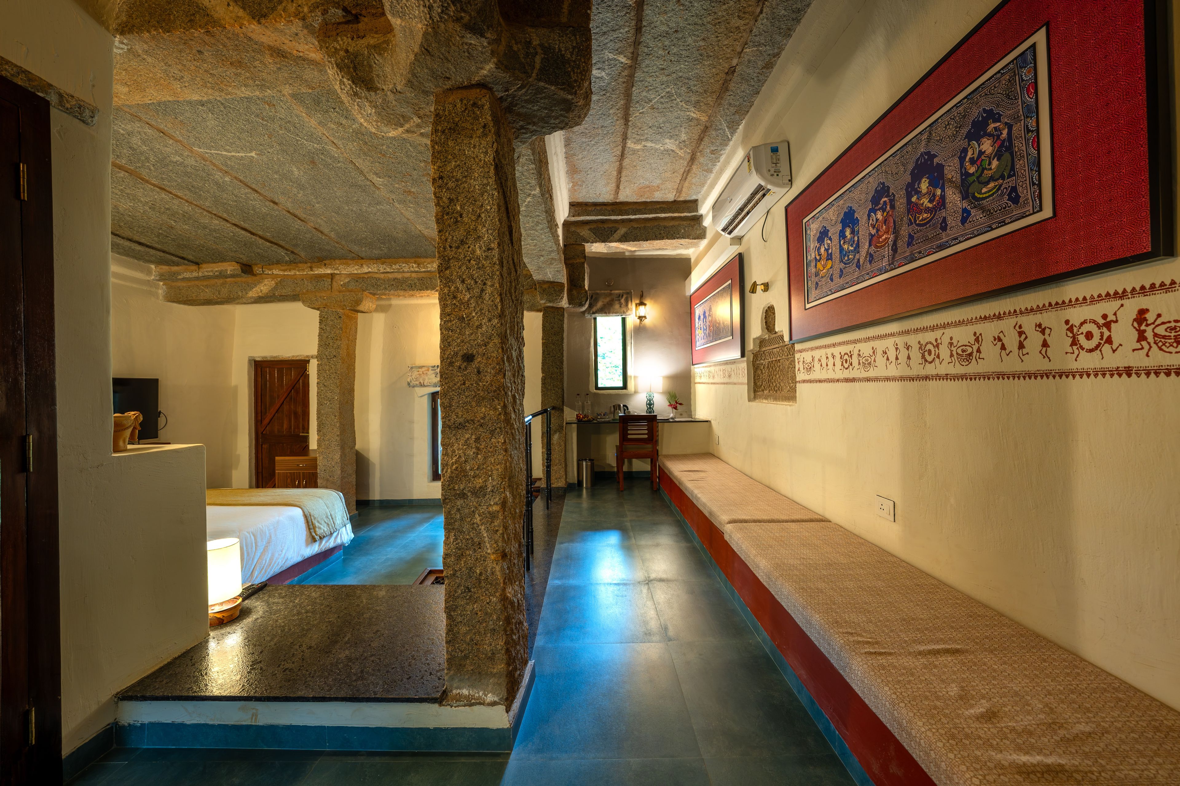 A corridor with stone columns, a bed, a desk, and a wall with traditional artwork.