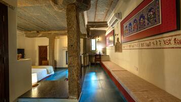 A corridor with stone columns, a bed, a desk, and a wall with traditional artwork.