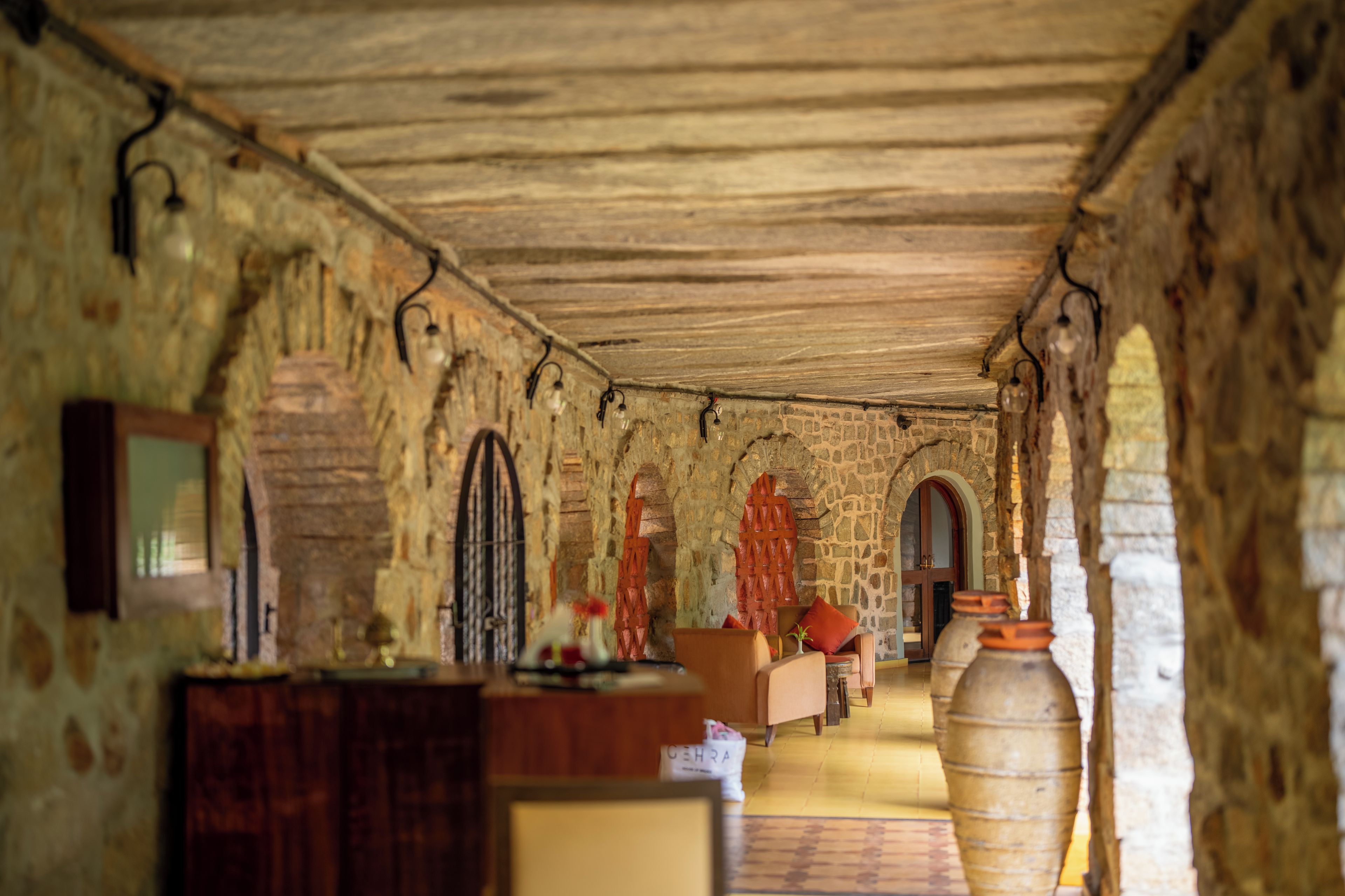 A corridor with stone walls, wooden ceiling, and arched doorways.