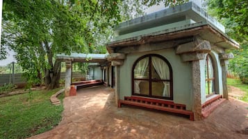 A small stone building with a bench and a window, surrounded by trees.