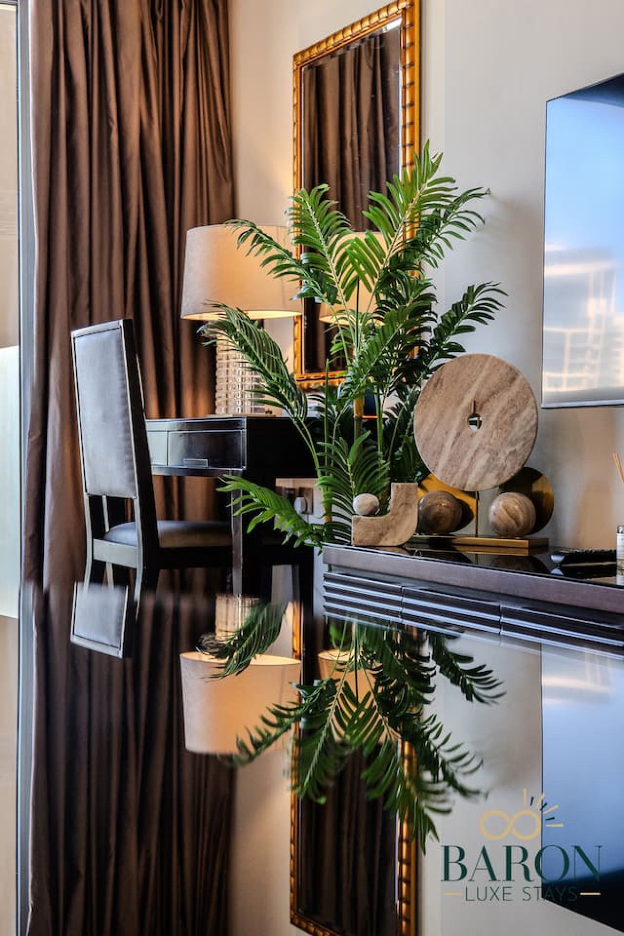 Un comedor moderno con una mesa reflectante, una silla, una lámpara y un arreglo decorativo de plantas.